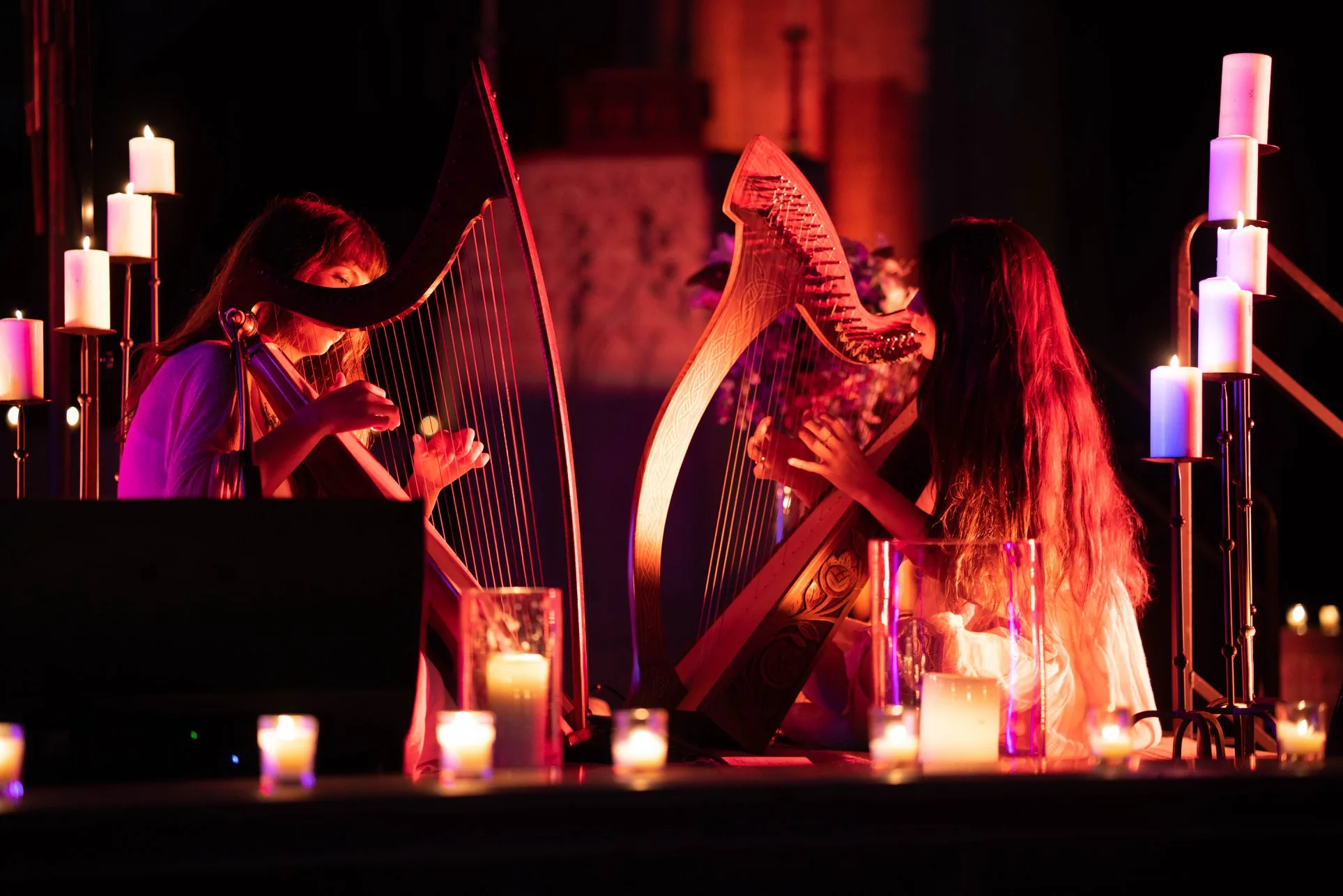 Sarah Glass and Alisa Rose Healy at their harps, face to face, inside their ring of candles on a night stage