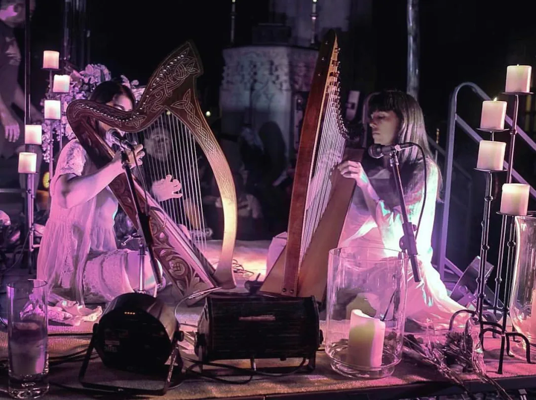 Sarah Glass and Alisa Rose Healy seated at their harps among candles on a night stage